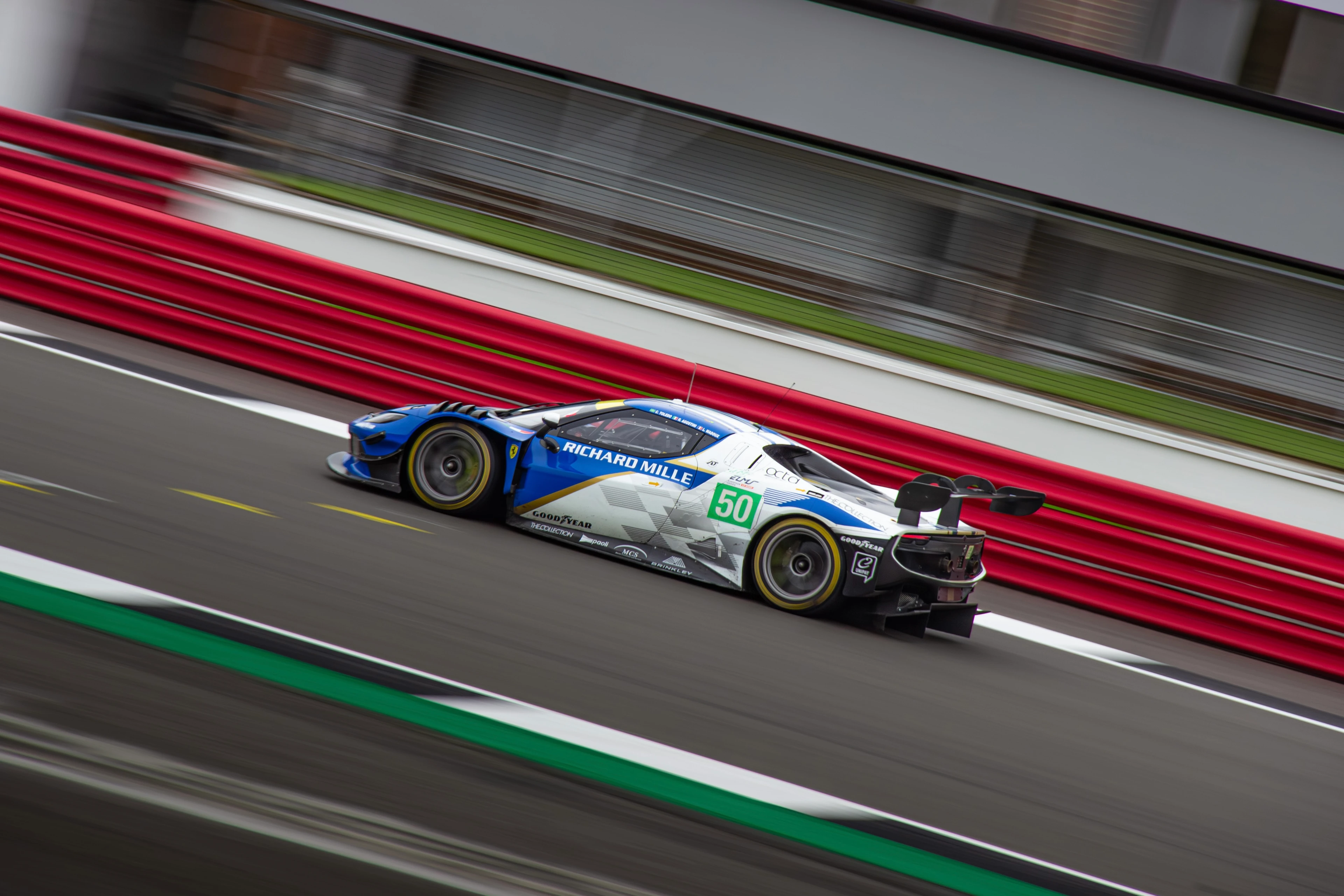 The blue and white number 50 Ferrari passes the barriers in a diagonal panning photograph.