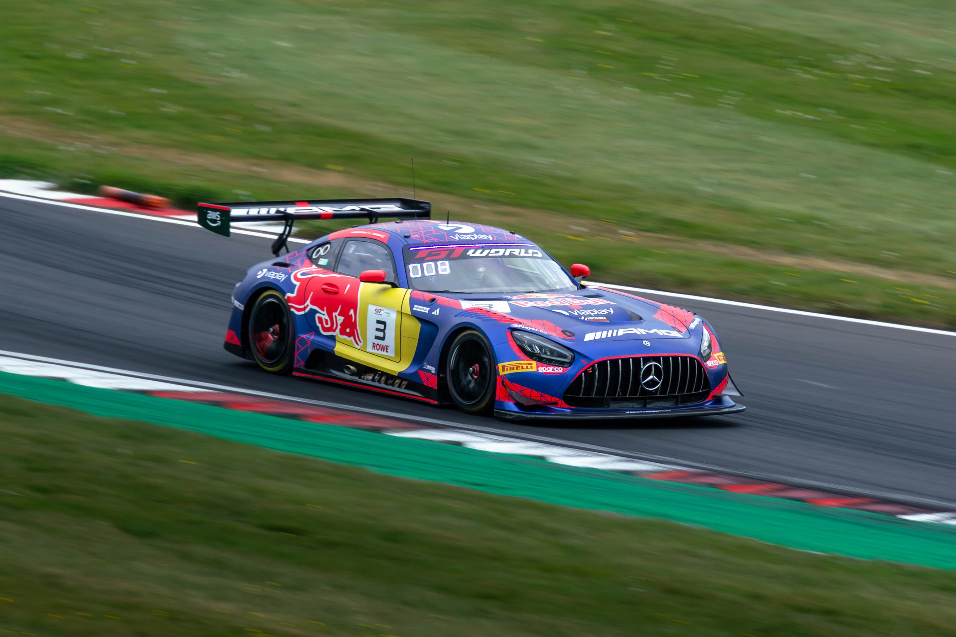 A blue and red Mercedes-AMG GT race car rides close to the kerb.